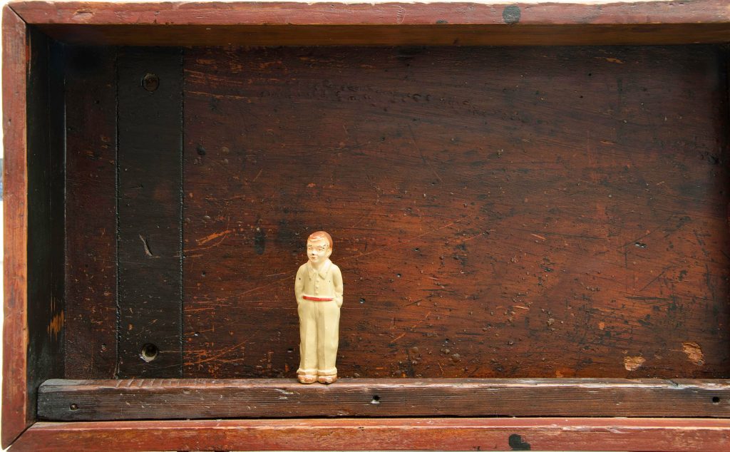 Tiny toy figure standing in a wooden shadow box