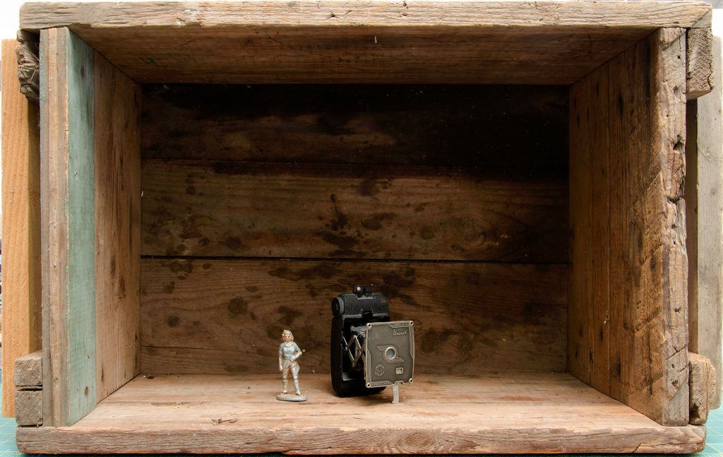 Tiny toy figure and antique camera in wooden shadow box
