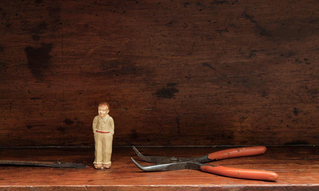 Tiny toy figure standing next to an old pair of pliers in a wooden shadow box