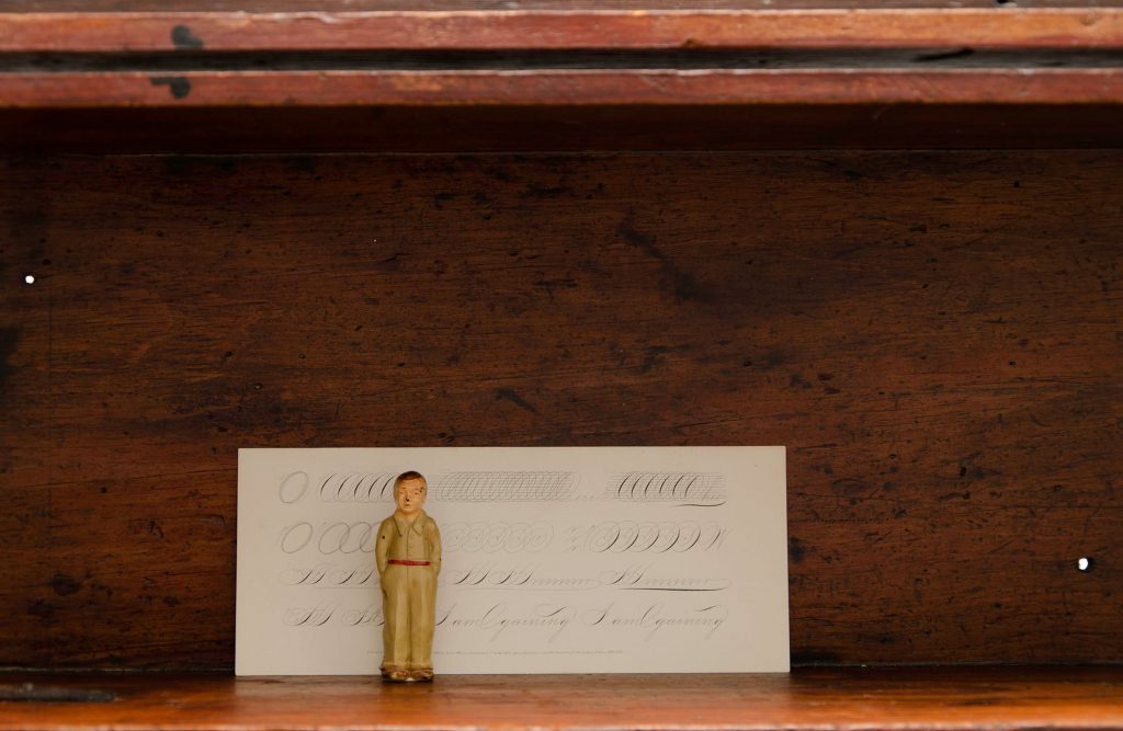 Tiny toy figure standing in front of a piece of white paper with ovals and handwriting in a wooden shadow box