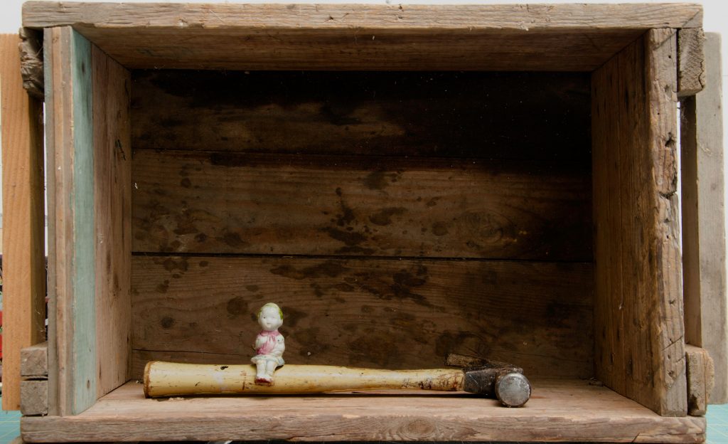 Tiny toy figure sitting on a hammer in a wooden shadow box